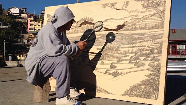 艺术家JordanMang-osan正在用放大镜在木板上作画